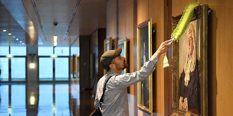 Matthew Smith, Collection Management Officer, cleans a portrait in the Members Hall ground floor area