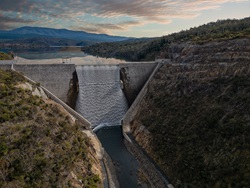 Aerial view of a dam with a lake and mountains in background