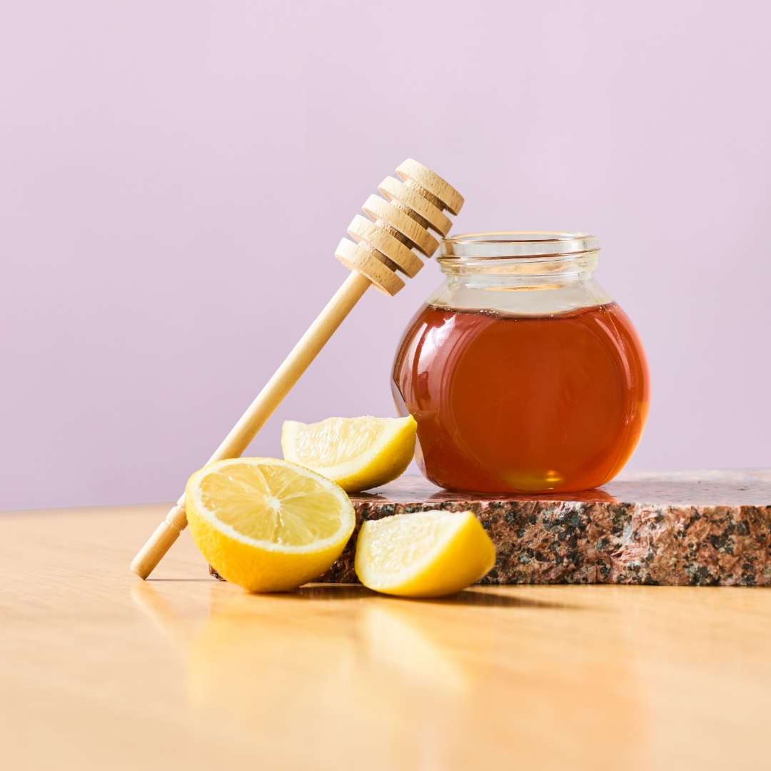 Photograph of a clear jar of honey with lemon wedges around it
