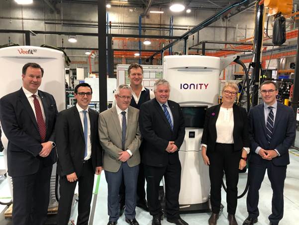 Photo 7: Committee members and tritium employees in front of some of the EV chargers manufactured by Tritium